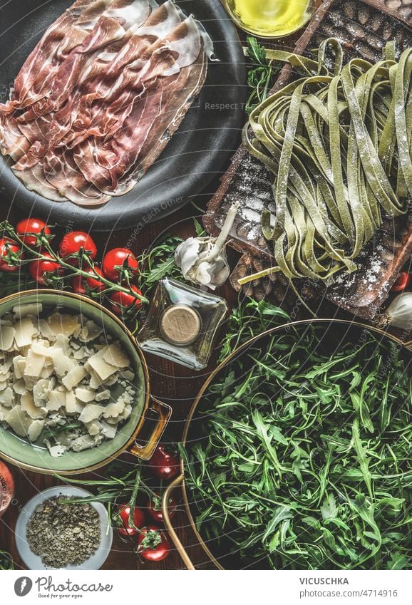 Italian food background with parma ham, green pasta, tomatoes, arugula , olive oil, herbs italian food garlic cooking traditional tagliatelle mediterranean food