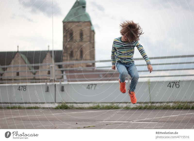 Child jumps into the air Playing urban Town Parking lot Concrete Action Exterior shot Fitness Empty Gray Movement move Dynamics out Hop Jump Tall fun Joy cloudy