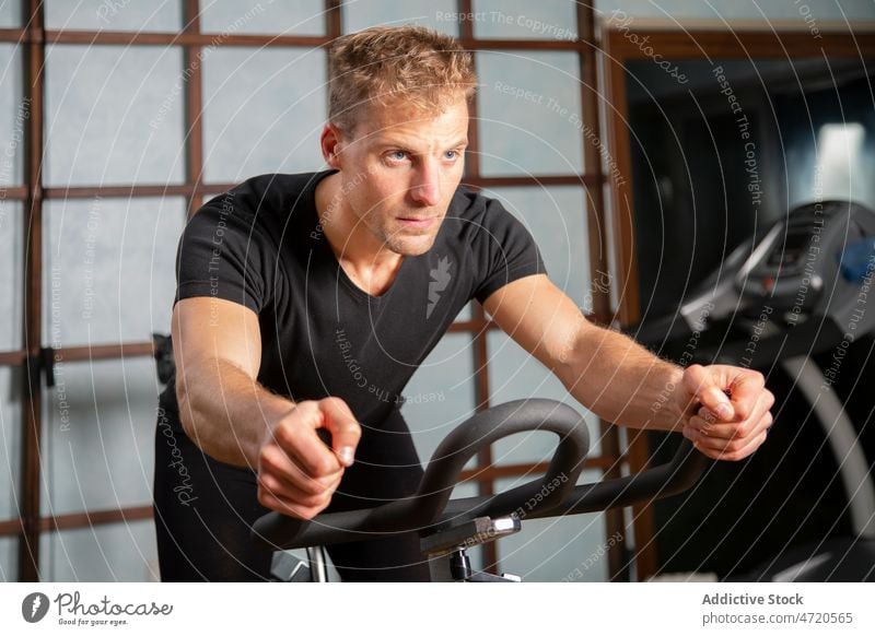 Confident man exercising on cycling machine in gym sportsman cycle exercise training workout determine confident fit male fitness athlete physical activity