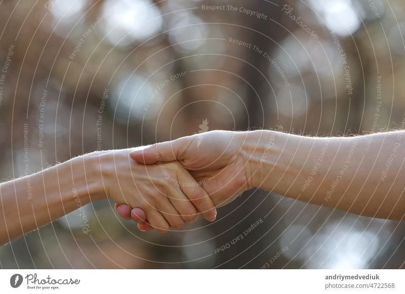 Handshake two people on the nature background. Close Up of female and male holding hands. Holding hands is a form of physical intimacy involving two or more people. It may or may not be romantic.