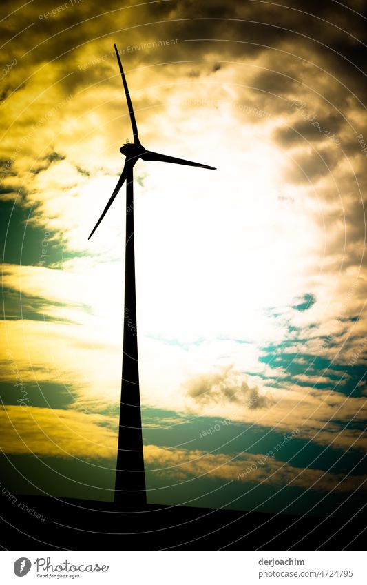 Full wind power ahead. A wind turbine stands in the strong yellow brown obscured edge of the sky.  The sun peeks out a little. Pinwheel Wind energy plant