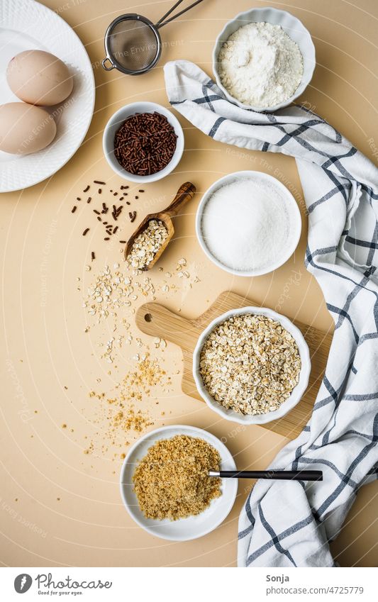 Baking ingredients in white bowls on a beige background. Top view. Ingredients Cake Preparation Flour eggs Sugar Oat flakes Breakfast Raw Cooking Table