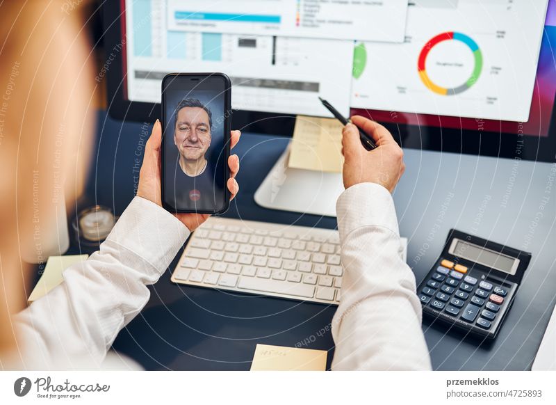Woman entrepreneur having business video chat on smartphone with her business partner. Businesswoman working with data on charts, graphs and diagrams on computer screen