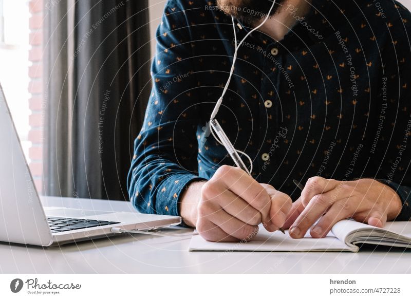 Man working at home and writing down his plan of action home office young adult worker lifestyles small business businessman laptop desk computer technology