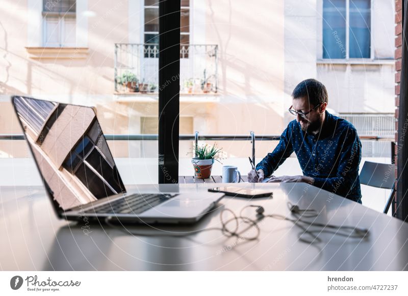 Man working at home and writing down his plan of action home office young adult worker lifestyles small business businessman laptop desk computer technology