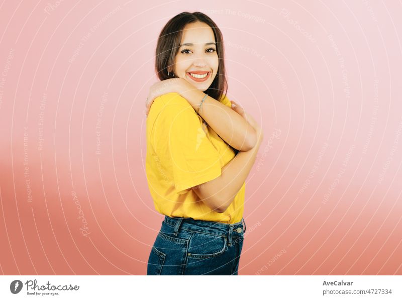Young woman embracing herself while smiling to camera, self love mental health feminism and woman power. Pink tone color background, expression of normal people. Mockup concept with people