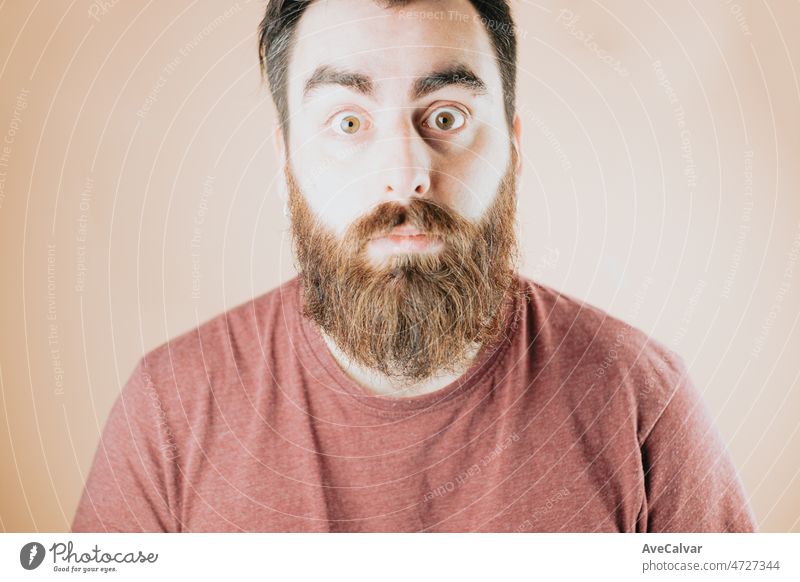 Young bearded handsome hipster man surprised and amazed, amazing news, unexpected reaction. Soft tone color background, expression of normal people. New deal new opportunity concept.