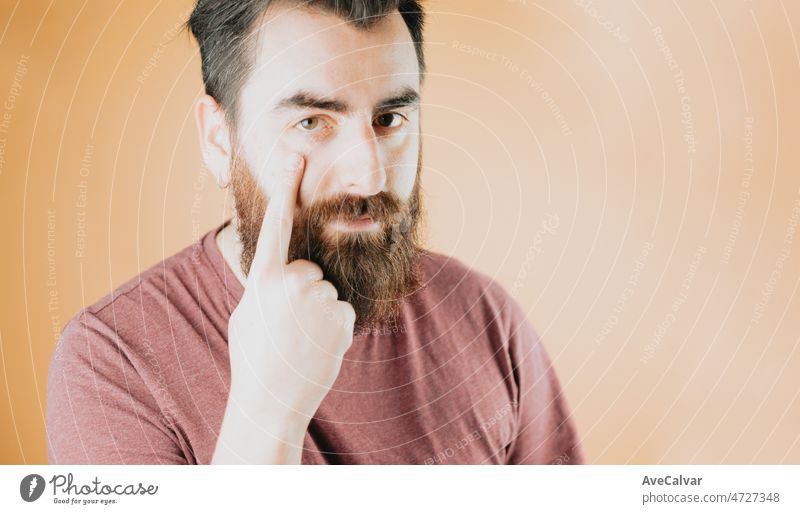 Close up portrait of a young handsome hipster man taking a look suspicious to camera. Inspecting distrust.Soft tone color background, expression of normal people.