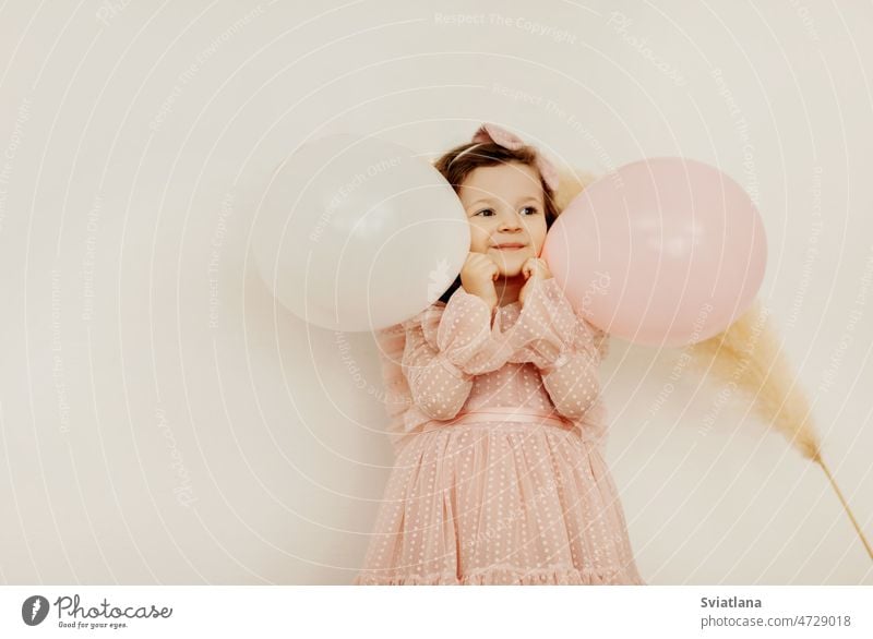 A charming little girl with balloons on her birthday has fun and laughs baby dress balls cute smile pink beautiful happy sweet light happiness child kid party