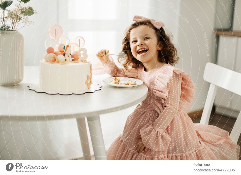 A laughing little girl eats a birthday cake on her birthday at home child pretty happy kid fun sweet food dessert beautiful party portrait childhood funny table