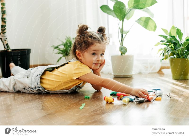 A charming little girl sculpts from colored plasticine on the floor. Home schooling, creative leisure with children baby play home making childrens creativity