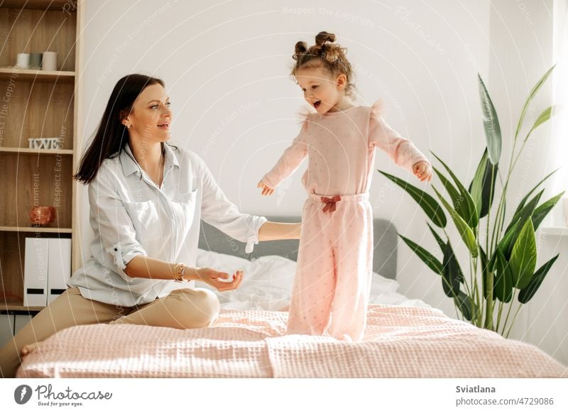 A young mother plays with her baby in the bedroom. Happy loving family. mom playing fun girl child happy portrait funny happiness healthy indoors joy joyful