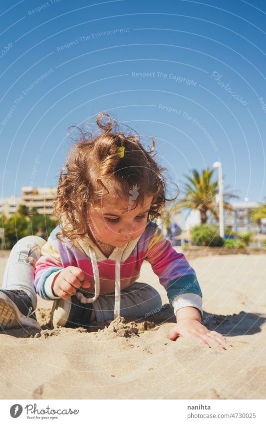 Young toddler playing with the sand at the beach alone enjoy summer explore parenting freedom happy rainbow happiness scene curly hair kid child baby childhood