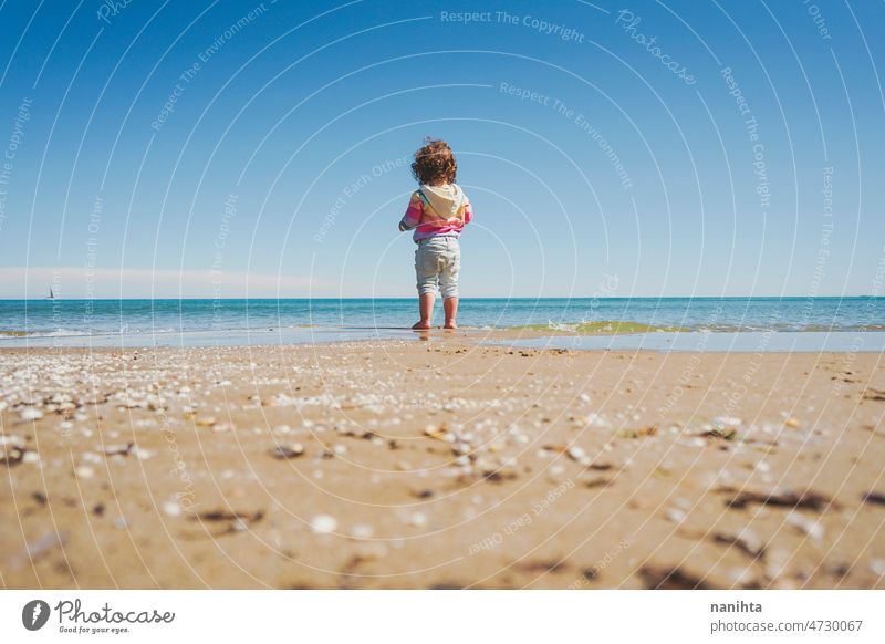 Wide view of a little girl wearing rainbow hoodie playing at the beach freedom happiness holidays baby toddler family sea shore playful real lifestyle people
