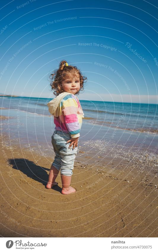 Wide view of a little girl wearing rainbow hoodie playing at the beach freedom happiness holidays baby toddler family sea shore playful real lifestyle people
