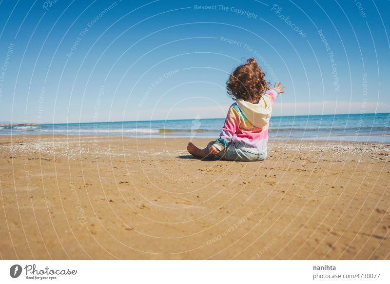 Wide view of a little girl wearing rainbow hoodie playing at the beach freedom happiness holidays baby toddler family sea shore playful real lifestyle people