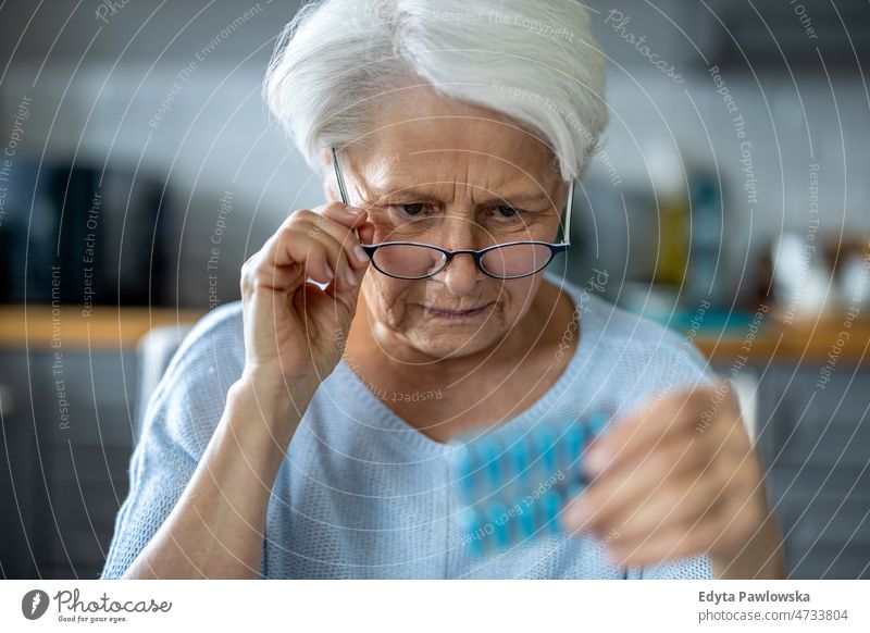 Senior woman about to take her medication pills glasses eyeglasses spectacles reading medicine prescription treatment drugs vitamin taking medicine pharmacy