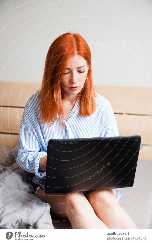 young work from home woman sitting on bed with laptop computer bedroom using typing business serious email real people notebook entertainment communication