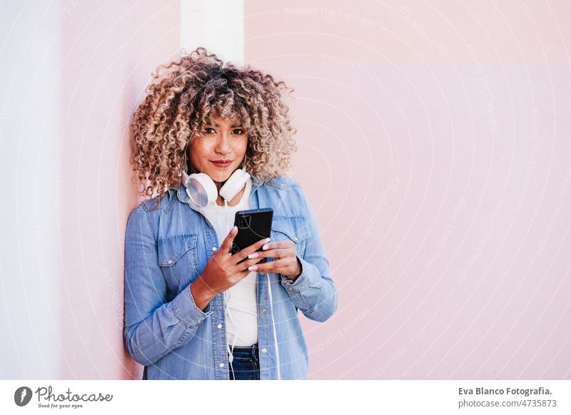 happy curvy hispanic woman with afro hair in city using mobile phone and headset. Body positivity listening body positivity technology internet wireless picture