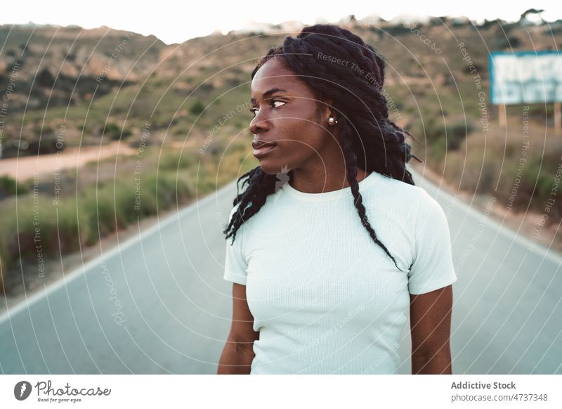 Black woman standing on empty road in mountains highland asphalt evening summer roadway female ethnic black african american peaceful carefree freedom route