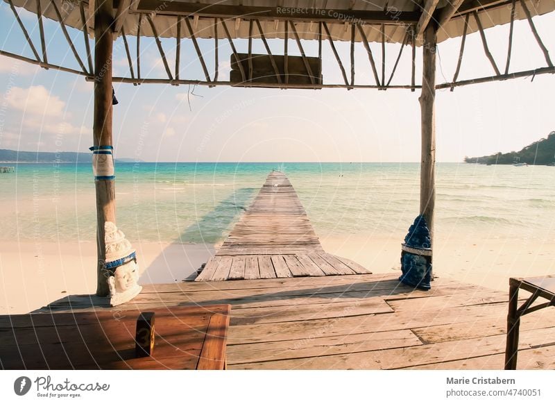 Scenic view from a gazebo of a wooden boardwalk leading to the white sandy beach of Koh Rong Samloen Island, a popular summer getaway destination in Cambodia