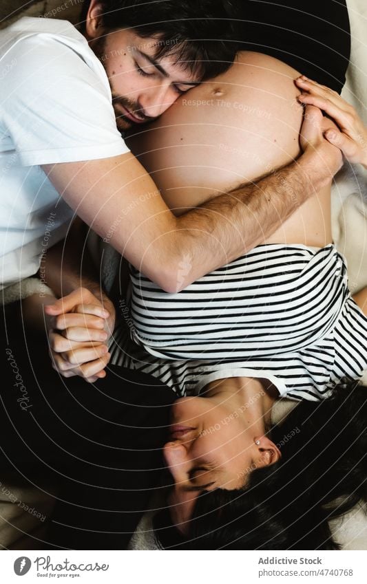 Tender man embracing pregnant woman on bed couple embrace hug belly love pregnancy lying tummy tender relationship together gentle relax home husband wife