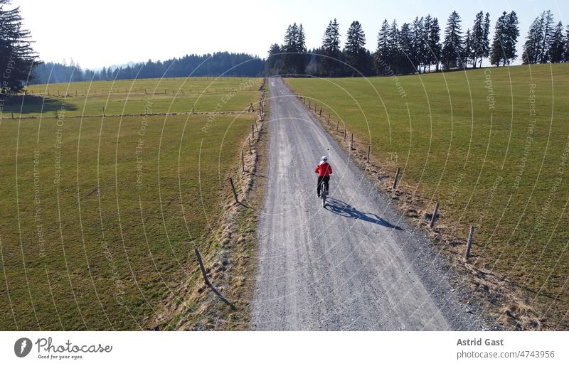 Aerial drone shot of female cyclist on lonely road with shadow Aerial photograph drone photo Spring Sports Cycling Bicycle Woman Driver Driving Street
