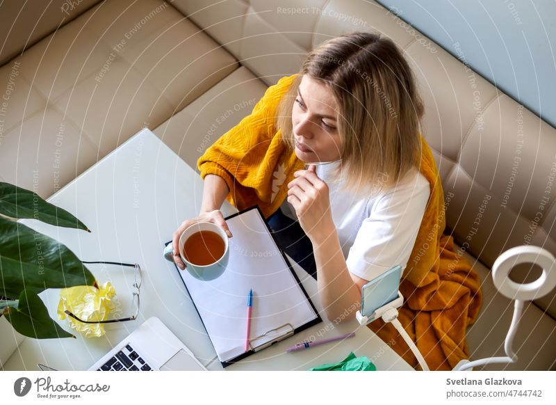 Work in progress. Blonde woman in yellow plaid work at home office on kitchen online chat using technology speaking video conference smartphone workplace