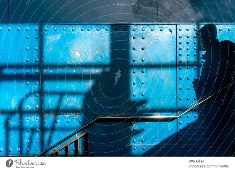 The shadow of a man on a very blue wall of metal, apparently on a staircase Blue Metal Stud Tin Steel Iron Colour Stairs rail Pattern Shadow Passer-by Man