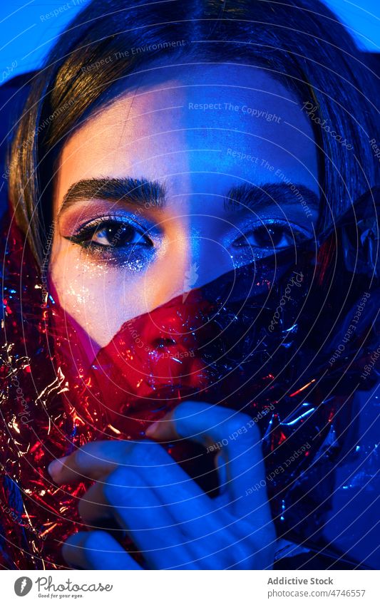 Fashionable woman wrapped in plastic in neon illumination model fashion provocative cool posture makeup female style blue light illuminate glow creative