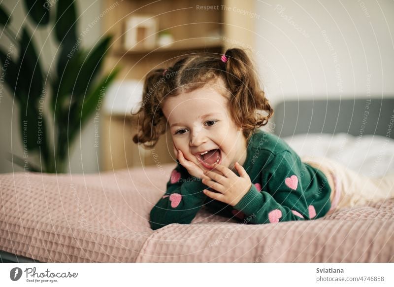 A cute little girl is lying on the bed with her leg raised and straightens  her panties - a Royalty Free Stock Photo from Photocase
