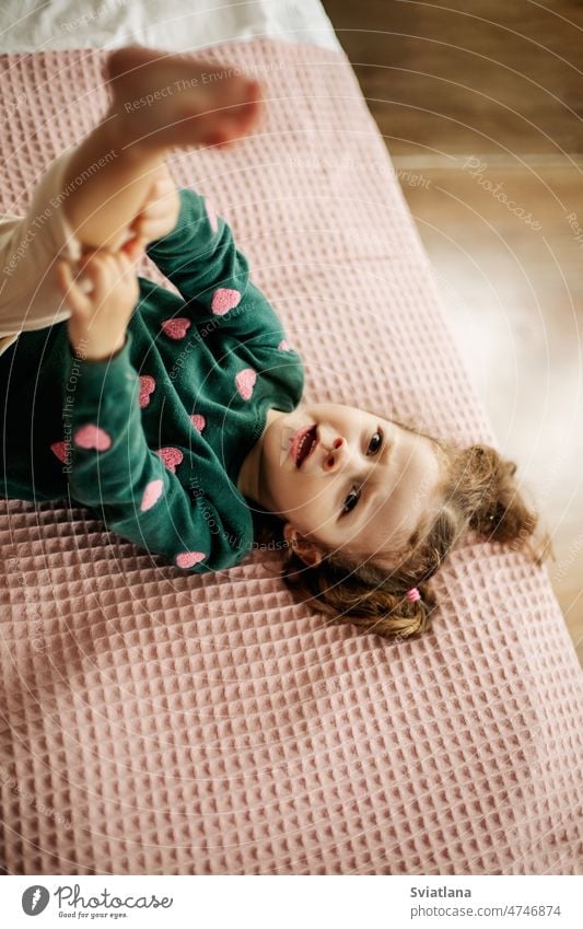 A cute little girl is lying on the bed with her leg raised and straightens  her panties - a Royalty Free Stock Photo from Photocase