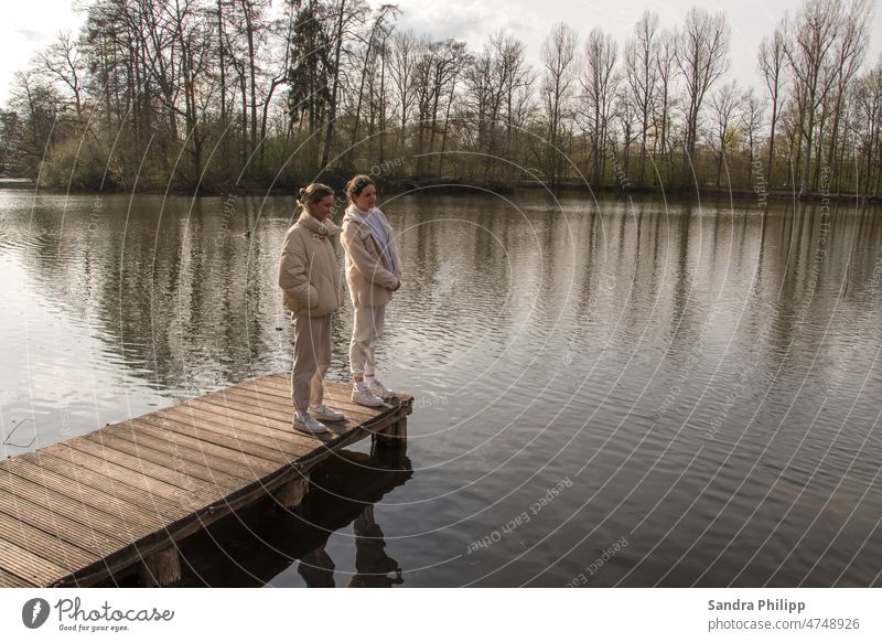 Two girls stand on a jetty and look at the water Water Footbridge Pond Blue Girl Lake Wood Calm Sky Exterior shot Relaxation Landscape Nature Colour photo