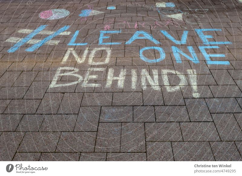 # LEAVE NO ONE BEHIND is written with street crayon in Ukrainian colors on a paved area Graffiti Paving stone Ukraine Solidarity Hope Conflict Humanity