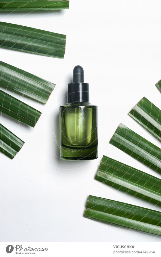 Green glass cosmetic bottle with pipette at white background with green palm leaves. skin care moisturizing face serum top view copy space beauty beauty product