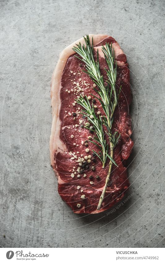 Raw beef steak with pepper and rosemary at grey background. raw seasoning meat flavorful ingredients top view angus barbecue beefsteak fillet food fresh home