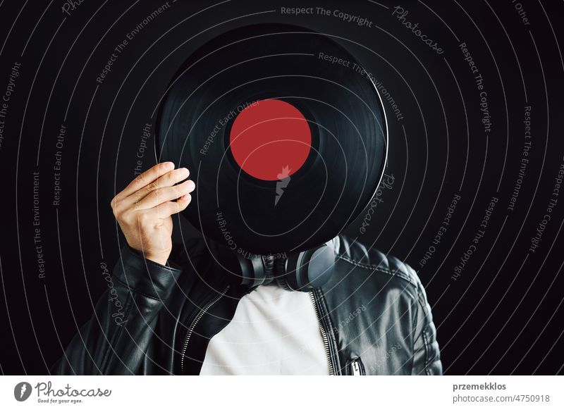 Man hiding behind retro vinyl record covering head. Rock style. Vintage music style. Male wearing black jacket holding vinyl record standing on black background. Retro music