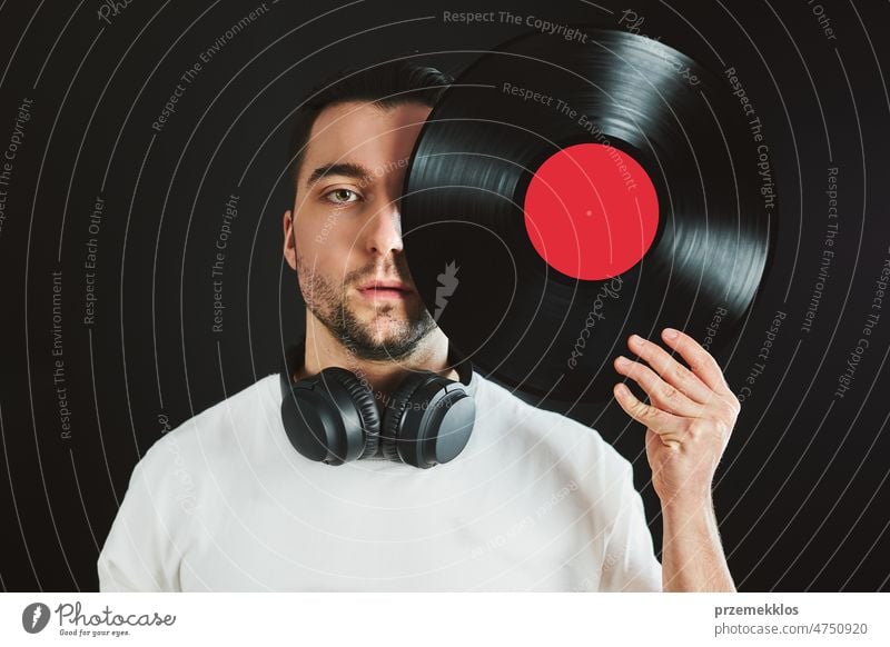 Man holding retro vinyl record covering face. Vintage music style. Male holding vinyl record disc standing on dark background. Retro music rock vintage analog