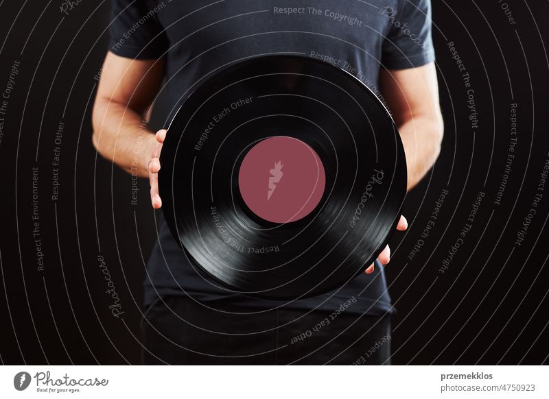 Man with vinyl record. Vintage music style. Male wearing blue t-shirt holding old music record standing on black background. Retro music disc retro vintage