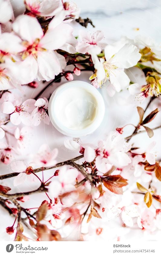 op view of cosmetic cream with pink cherry flowers in a blue glass jar. Hygienic skincare lotion product.Idioma de palabras top view hygienic almonds spa