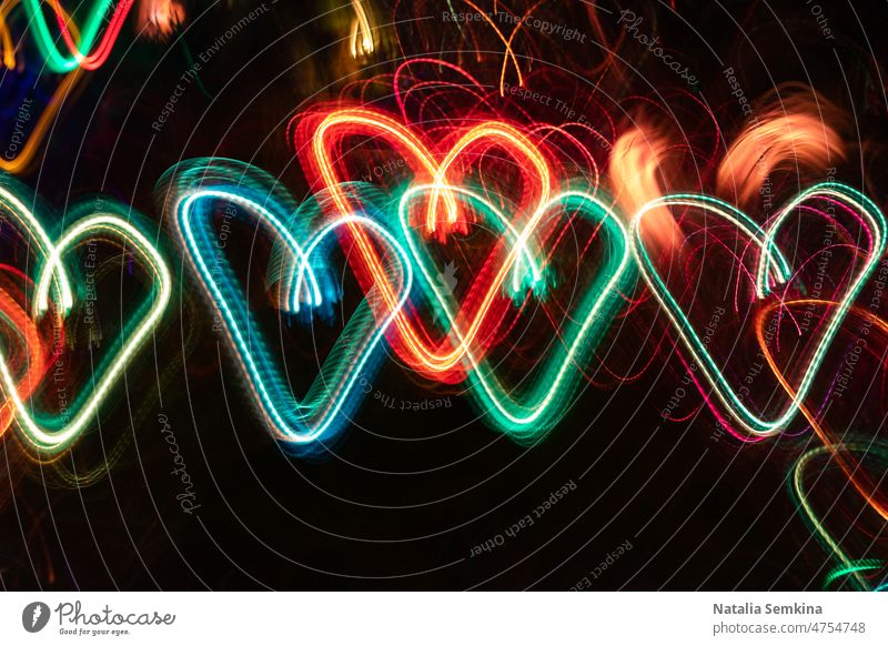 Row of multicolored neon glowing hearts on black background. long exposure laser abstract bright orange party pattern power ray row shiny slinky splash springs
