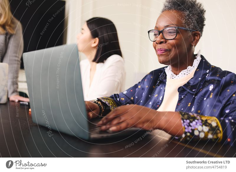 Portrait of senior black businesswoman with short gray hair wearing glasses and using laptop portrait eyeglasses smile happy meeting boardroom three adult