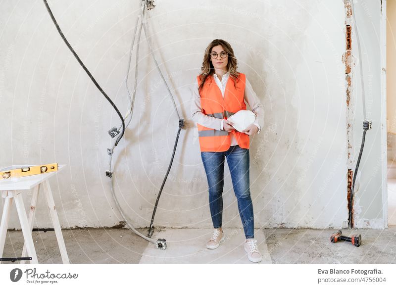 professional confident architect woman in construction site holding blueprints. Home renovation workspace protective helmet protective jacket real estate