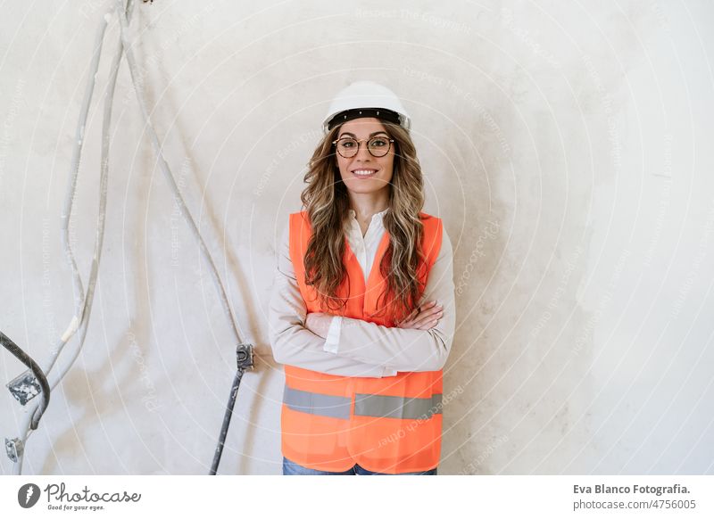 professional confident architect woman in construction site with arms crossed. Home renovation blueprints workspace protective helmet protective jacket
