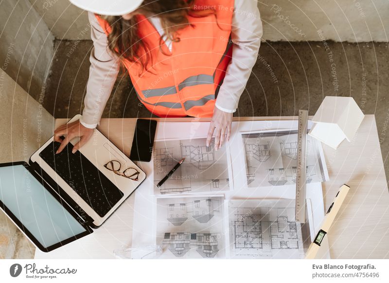 top view of professional architect woman in construction site working on laptop and blueprints unrecognizable mobile phone workspace protective helmet