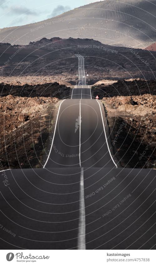 Endless road on a volcano in Timanfaya National Park in Lanzarote in the Canary Islands with a continuous line, black volcanic rocks on the side and volcanoes in mist in background.