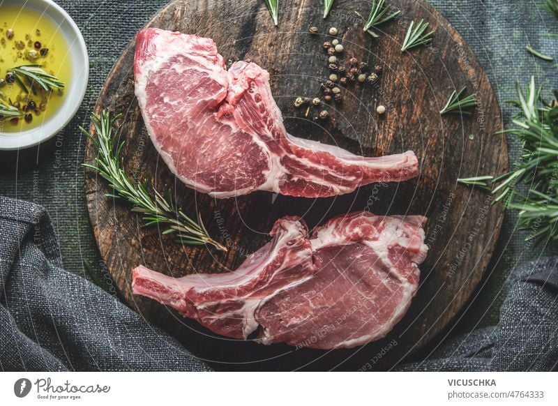 Two raw pork cutlets on wooden cutting board with rosemary on dark kitchen table with  olive oil. pepper cooking preparation meat top view spices herbs barbecue