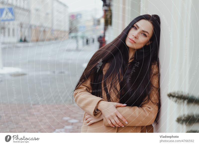 Young brunette woman in beige winter coat stands alone on the