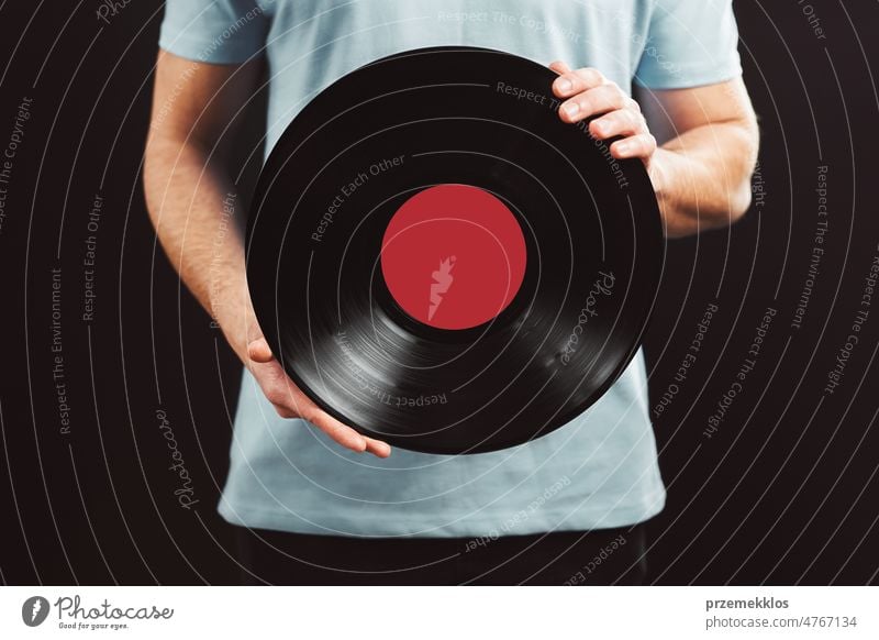 Man with vinyl record. Vintage music style. Male wearing blue t-shirt holding black analog disk standing on black background. Retro music vintage disc retro