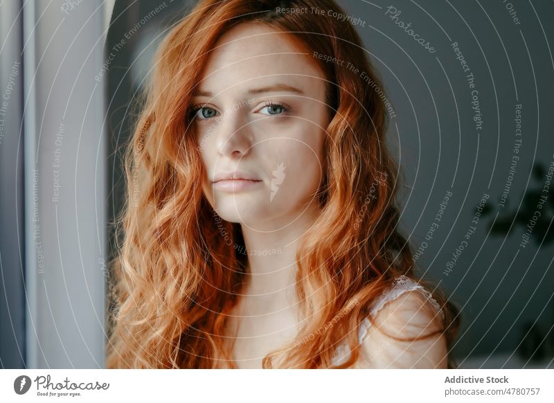 Sad redhead woman looking at camera in room window melancholy thoughtful dreamy sad lonely solitude pensive home tranquil curly hair domestic peaceful female